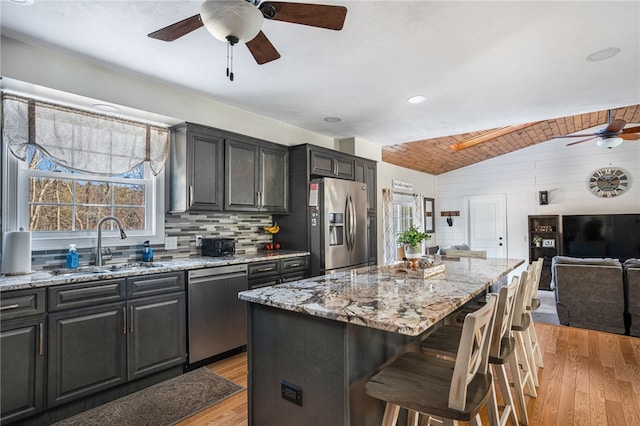 kitchen featuring a kitchen bar, sink, light stone counters, a center island, and appliances with stainless steel finishes