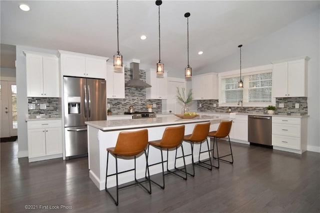 kitchen with white cabinets, stainless steel appliances, vaulted ceiling, and wall chimney range hood