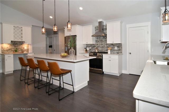 kitchen featuring lofted ceiling, wall chimney range hood, pendant lighting, stainless steel appliances, and white cabinets