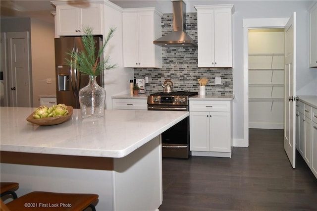 kitchen featuring white cabinetry, tasteful backsplash, appliances with stainless steel finishes, dark hardwood / wood-style flooring, and wall chimney range hood