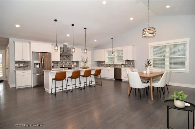 kitchen featuring vaulted ceiling, a kitchen island, white cabinetry, stainless steel appliances, and wall chimney range hood