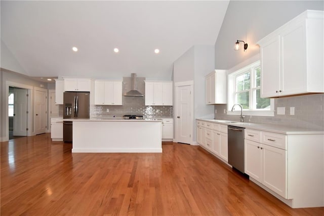 kitchen featuring wall chimney exhaust hood, white cabinetry, a center island, vaulted ceiling, and appliances with stainless steel finishes