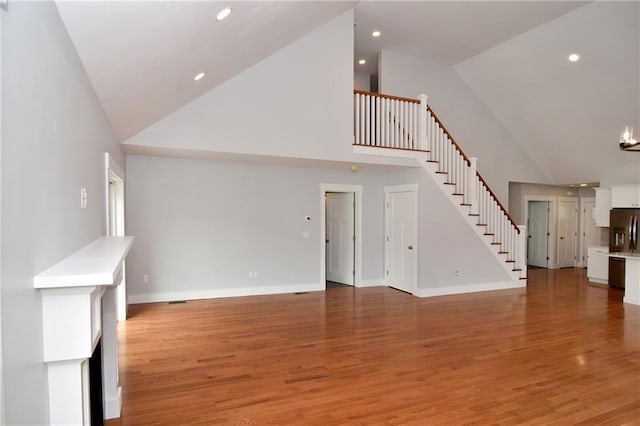 unfurnished living room with hardwood / wood-style flooring, a chandelier, and high vaulted ceiling