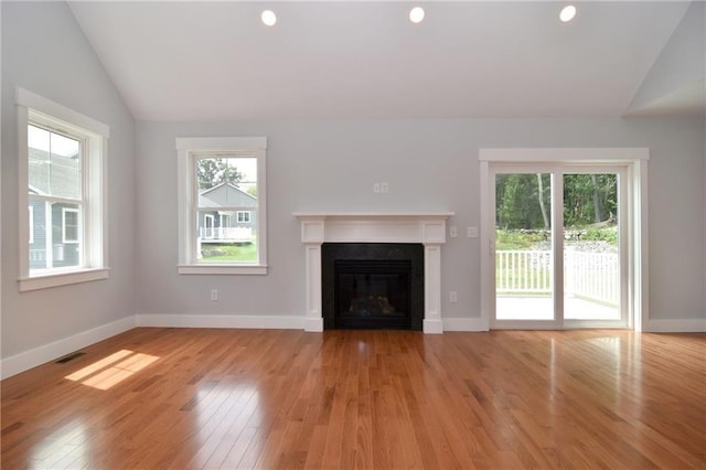 unfurnished living room with lofted ceiling, a wealth of natural light, and light wood-type flooring