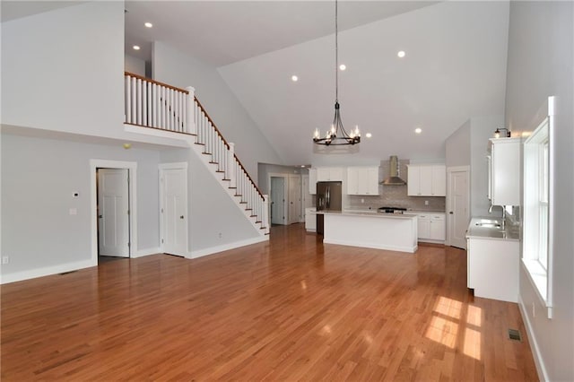 unfurnished living room with sink, a notable chandelier, high vaulted ceiling, and light hardwood / wood-style floors