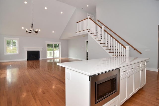 kitchen featuring hanging light fixtures, high vaulted ceiling, stainless steel microwave, white cabinets, and a kitchen island