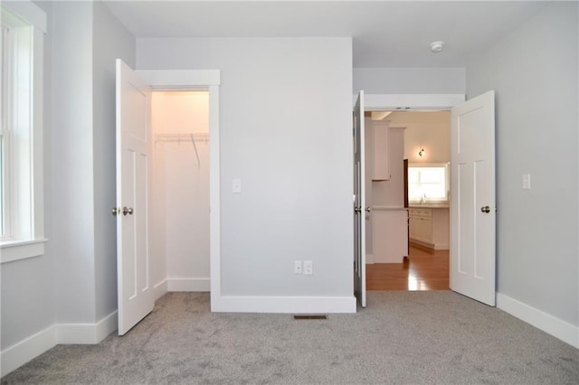 unfurnished bedroom featuring a walk in closet, light colored carpet, and a closet