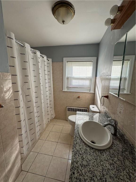 bathroom featuring curtained shower, radiator heating unit, tile walls, tile patterned flooring, and toilet