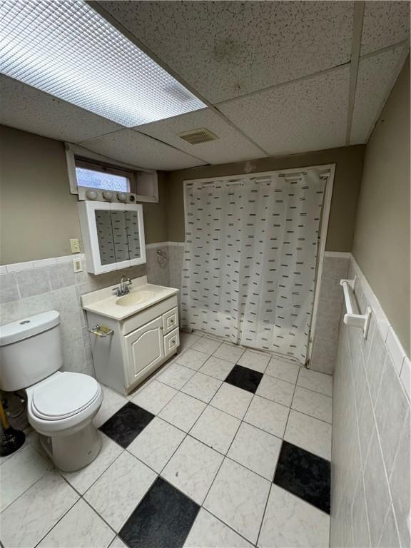 bathroom with tile patterned floors, tile walls, and a drop ceiling