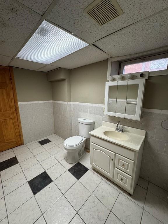 bathroom featuring vanity, tile patterned flooring, tile walls, and a drop ceiling