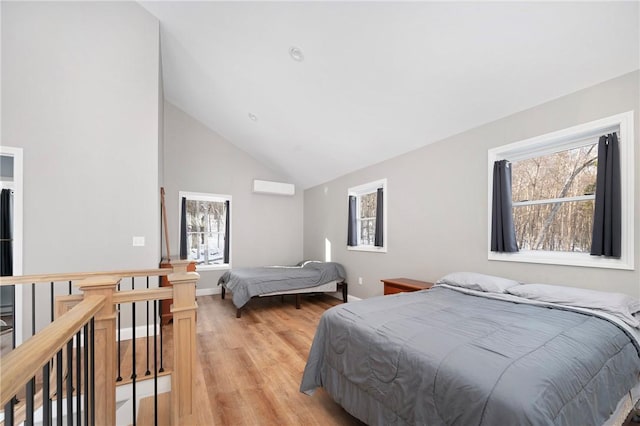 bedroom featuring an AC wall unit, vaulted ceiling, multiple windows, and light wood-type flooring