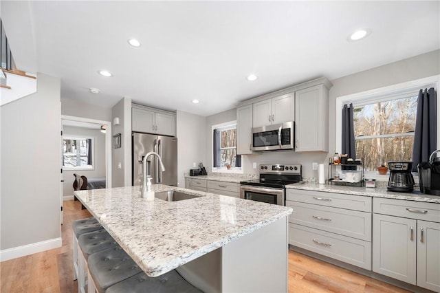 kitchen with appliances with stainless steel finishes, sink, a kitchen bar, a kitchen island with sink, and light stone countertops