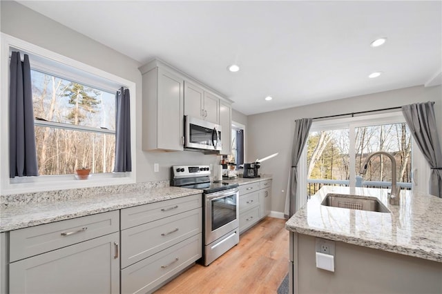 kitchen featuring sink, gray cabinetry, light stone counters, light hardwood / wood-style floors, and stainless steel appliances