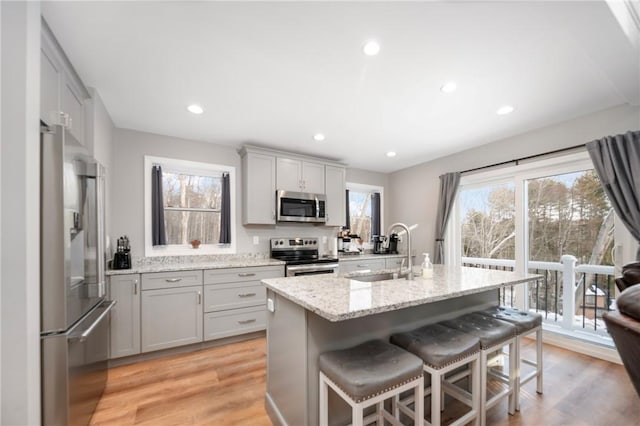 kitchen featuring a breakfast bar, sink, light hardwood / wood-style flooring, a center island with sink, and appliances with stainless steel finishes