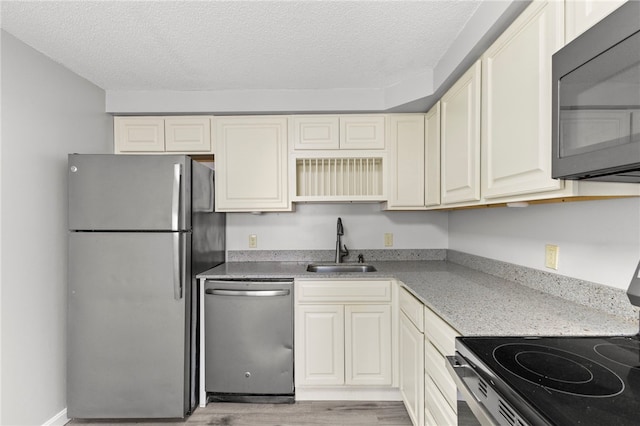 kitchen featuring stainless steel appliances, sink, a textured ceiling, and light hardwood / wood-style flooring