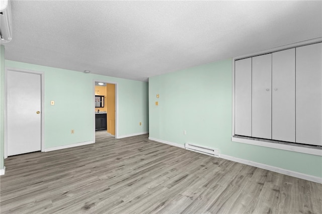 unfurnished room featuring a baseboard heating unit, light hardwood / wood-style flooring, and a textured ceiling