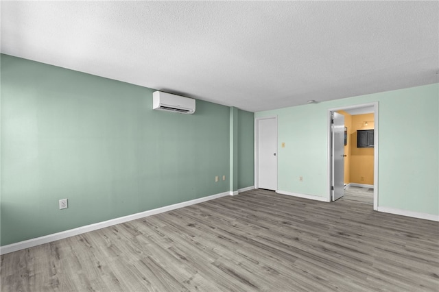 empty room with wood-type flooring, a wall unit AC, and a textured ceiling