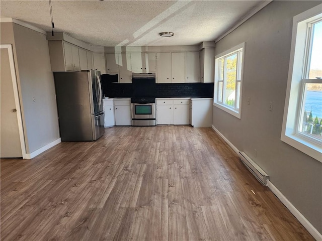 kitchen with appliances with stainless steel finishes, a baseboard heating unit, white cabinets, decorative backsplash, and light wood-type flooring