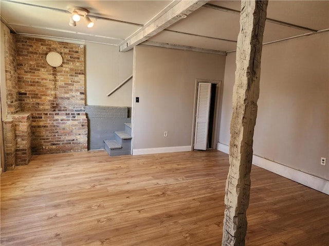 empty room with beamed ceiling, brick wall, and light hardwood / wood-style flooring