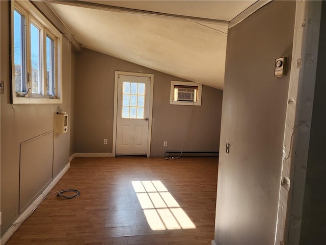 doorway to outside featuring vaulted ceiling, hardwood / wood-style floors, a wealth of natural light, a wall mounted air conditioner, and a baseboard radiator