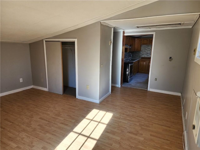 unfurnished bedroom with sink, light hardwood / wood-style floors, vaulted ceiling, and a closet