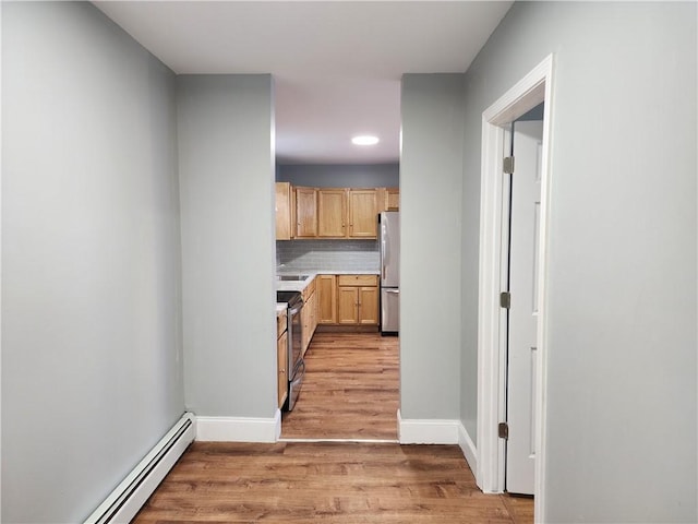 kitchen with light hardwood / wood-style flooring, backsplash, stainless steel appliances, a baseboard radiator, and light brown cabinets