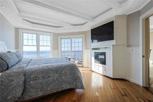 bedroom featuring beamed ceiling, a wainscoted wall, a glass covered fireplace, and wood-type flooring