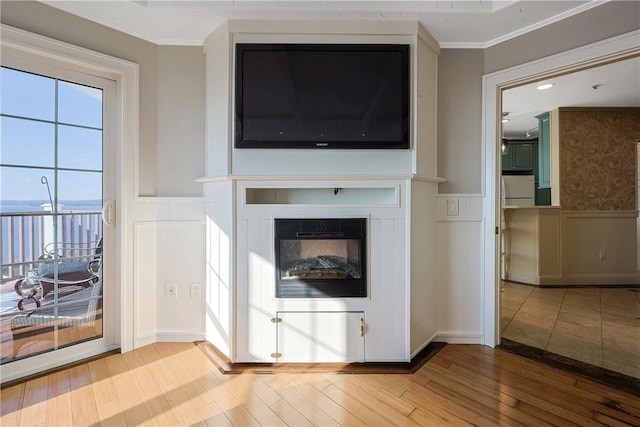 unfurnished living room featuring wood finished floors, a wainscoted wall, ornamental molding, a glass covered fireplace, and a decorative wall