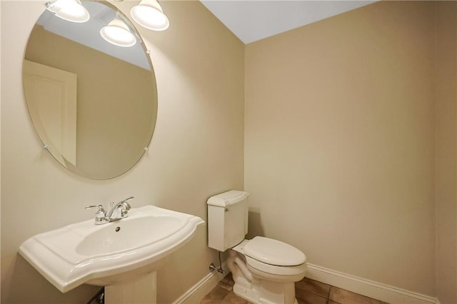 half bathroom featuring tile patterned floors, toilet, baseboards, and a sink