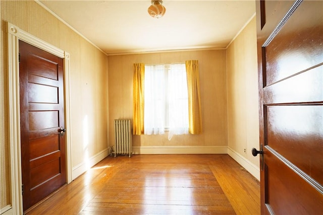 spare room with crown molding, radiator, and light wood-type flooring