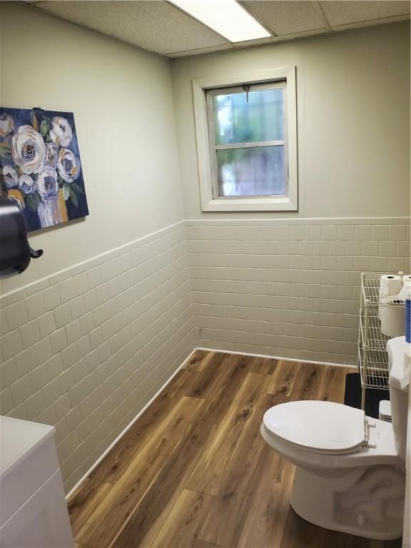 bathroom featuring hardwood / wood-style flooring, a paneled ceiling, tile walls, and toilet