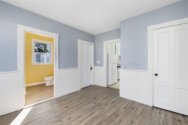 unfurnished bedroom featuring ensuite bath, light hardwood / wood-style floors, and white refrigerator