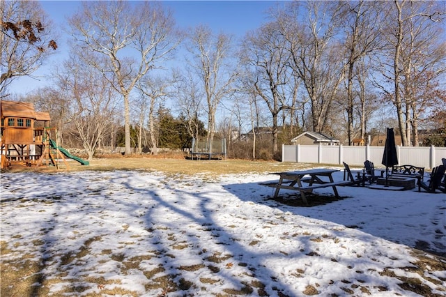 yard layered in snow with a playground and a trampoline