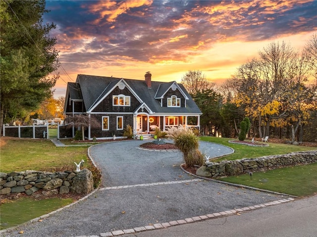 shingle-style home with driveway, a front lawn, a chimney, and fence