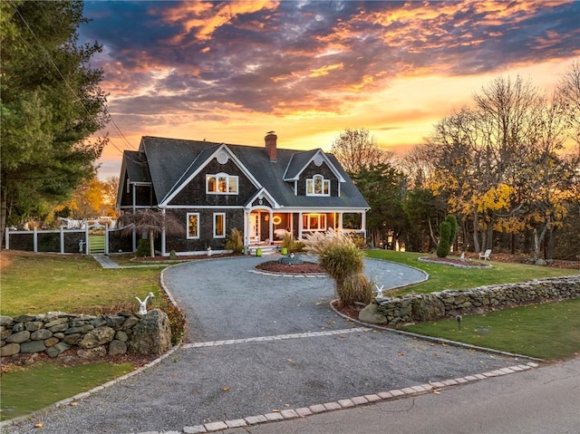shingle-style home featuring curved driveway, fence, a front lawn, and a chimney