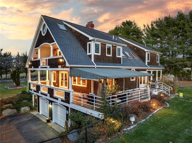 back house at dusk with a garage and a balcony