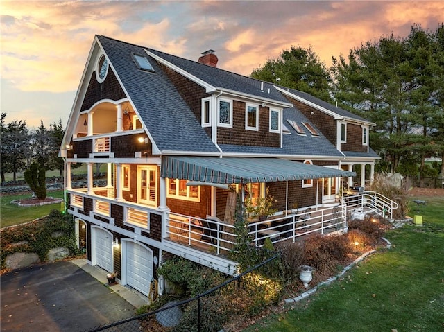 shingle-style home featuring a porch, a garage, a shingled roof, driveway, and a chimney