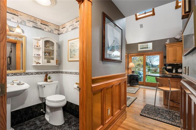 bathroom featuring lofted ceiling, sink, wood-type flooring, toilet, and a wood stove