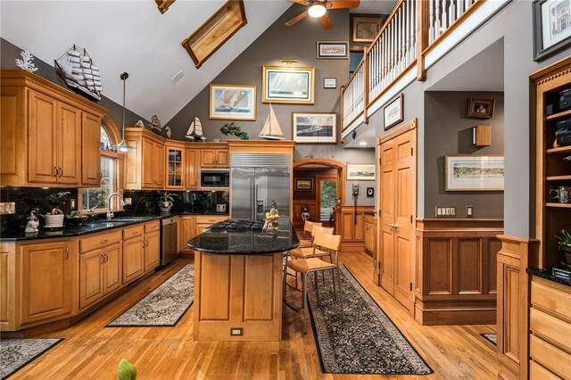 kitchen with a breakfast bar area, built in appliances, a kitchen island, decorative light fixtures, and light wood-type flooring