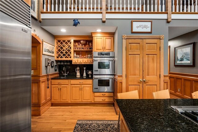 kitchen featuring dark stone countertops, light hardwood / wood-style floors, a high ceiling, and appliances with stainless steel finishes