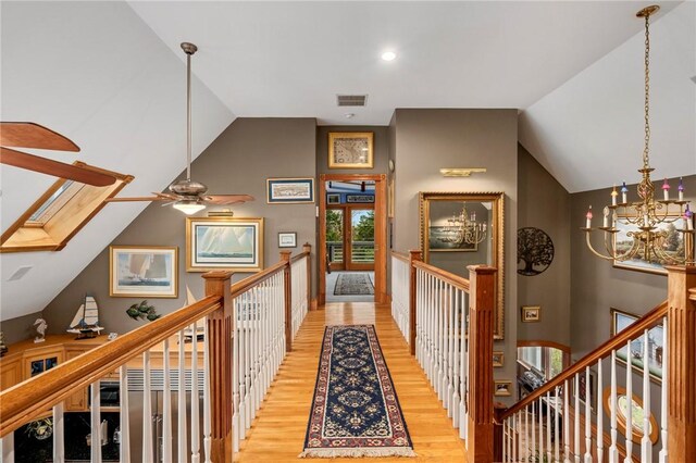 hallway with vaulted ceiling with skylight, light hardwood / wood-style flooring, and a notable chandelier