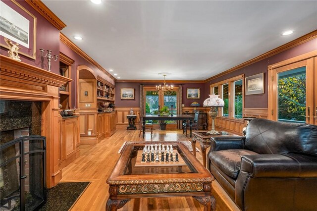 living room featuring ornamental molding, a notable chandelier, a fireplace, and light hardwood / wood-style floors