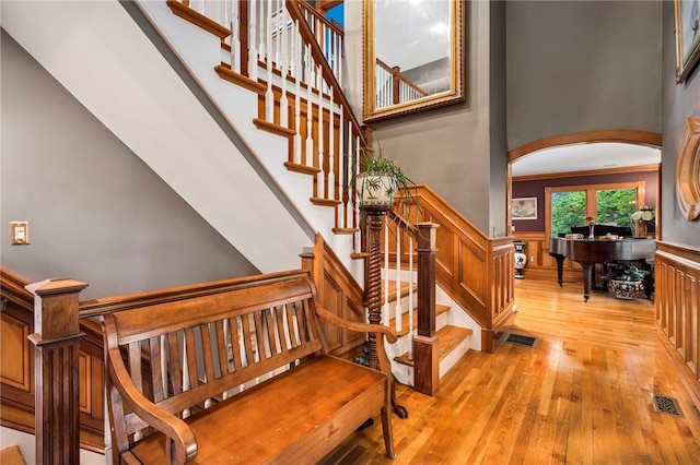 stairs featuring a wainscoted wall, visible vents, arched walkways, and wood finished floors