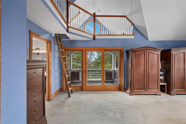 unfurnished living room featuring light carpet, high vaulted ceiling, and baseboards