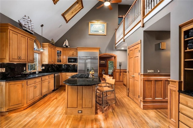 kitchen featuring arched walkways, brown cabinetry, wainscoting, built in appliances, and a kitchen bar