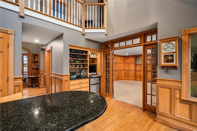 kitchen featuring a high ceiling, french doors, wainscoting, light wood-type flooring, and dark stone countertops