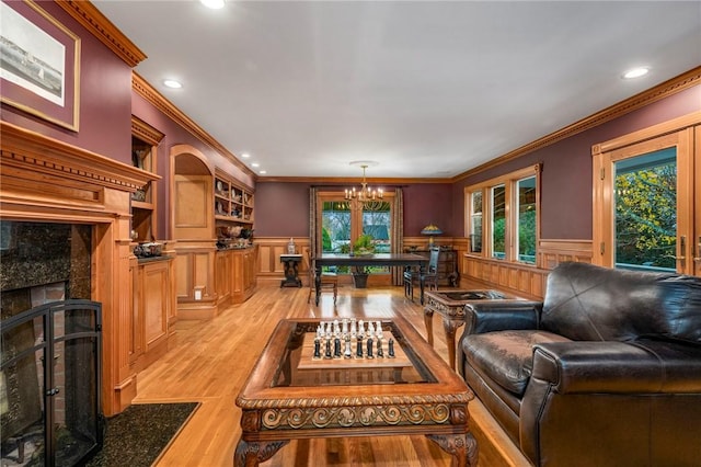 living area with a chandelier, light wood-style flooring, a premium fireplace, ornamental molding, and wainscoting