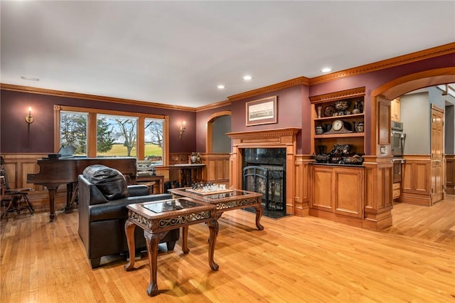 living room featuring a wainscoted wall, light wood-style flooring, a fireplace, and arched walkways