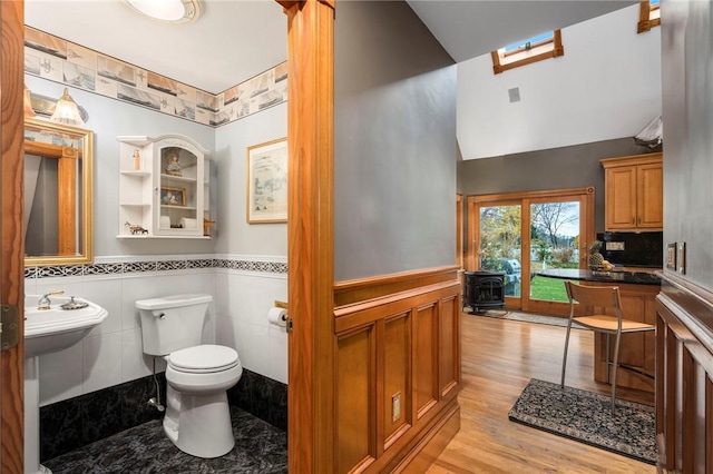 half bathroom with lofted ceiling, toilet, a wood stove, wainscoting, and wood finished floors