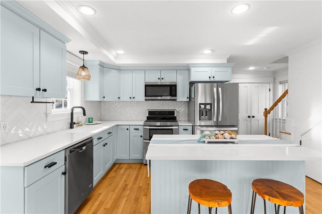 kitchen featuring a breakfast bar, decorative light fixtures, stainless steel appliances, crown molding, and light countertops